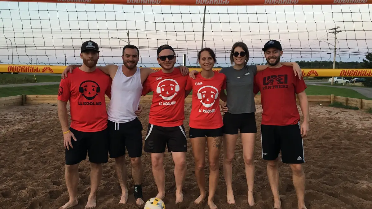 A beach volleyball team in red shirts lined up at the net on the sand