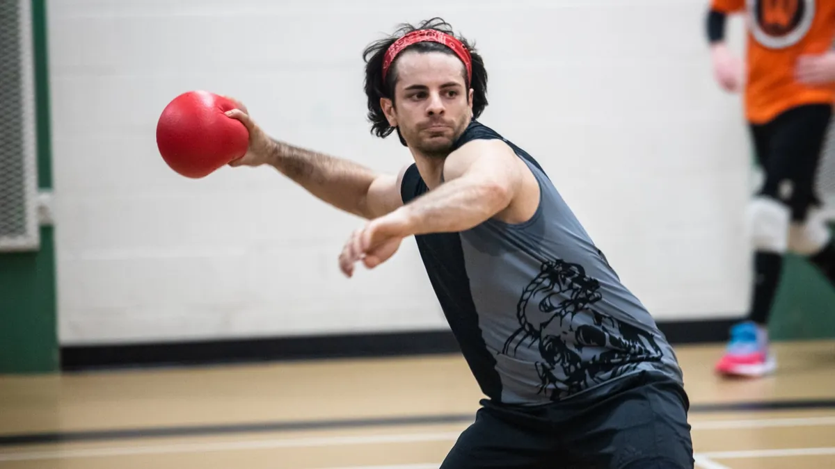 Dodgeball player winding up to throw a red ball, other players behind