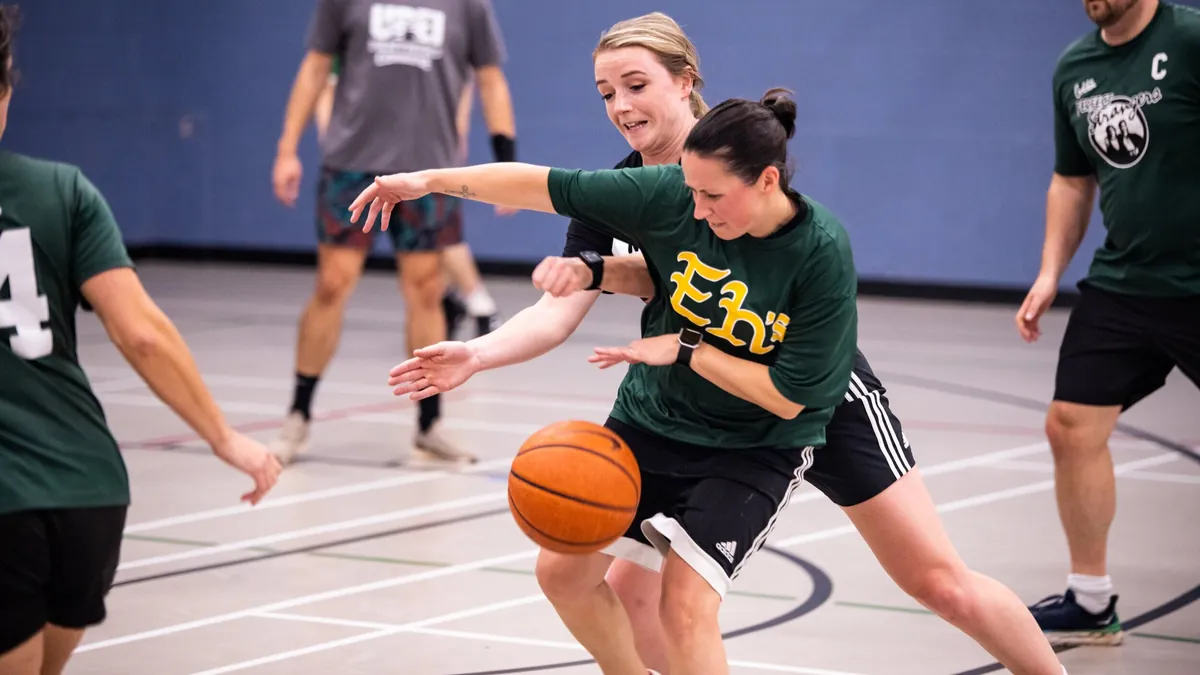 Woman in a green shirt dribbling a basketball past defenders on a multisport night