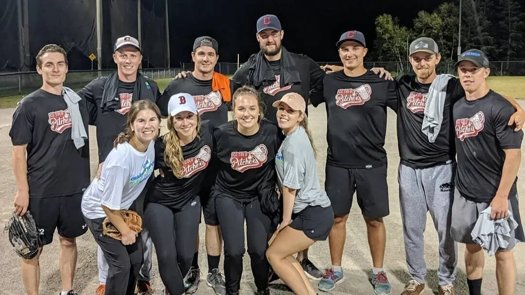A softball team in matching black shirts at the field at night