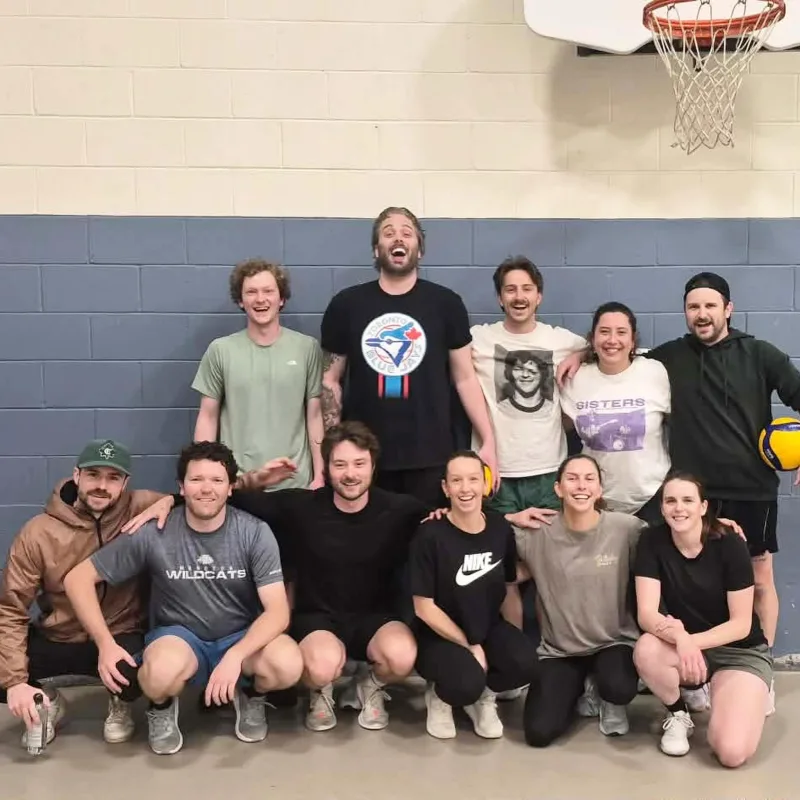 Spring 2026 champions: twelve players posing against a blue block wall under a basketball hoop, laughing
